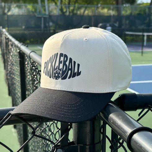 White and black cap with 'Pickleball' text on a tennis court